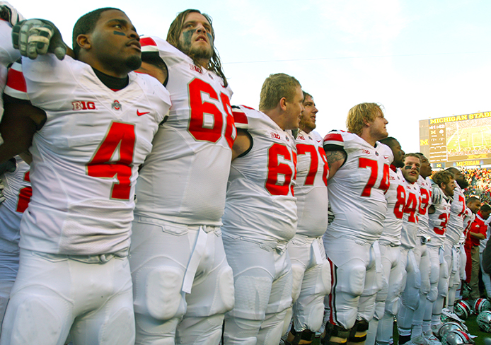 Redshirt-senior safety C.J. Barnett (4) stands with his teammates at the end of the game against Michigan Nov. 30 during ‘Carmen Ohio.’ OSU won, 42-41. Credit: Shelby Lum / Photo editor