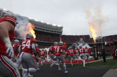 Ohio State football players running out onto to the field in front of scarlet crowd in Ohio Stadium.