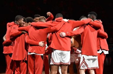 Ohio State men's basketball team huddle together at mid-court under a spotlight before a game