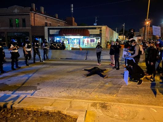 A protester lays on the road between police and a group of protesters on North High Street, south of Fifth Avenue. Credit: Max Garrison | Asst. Campus Editor