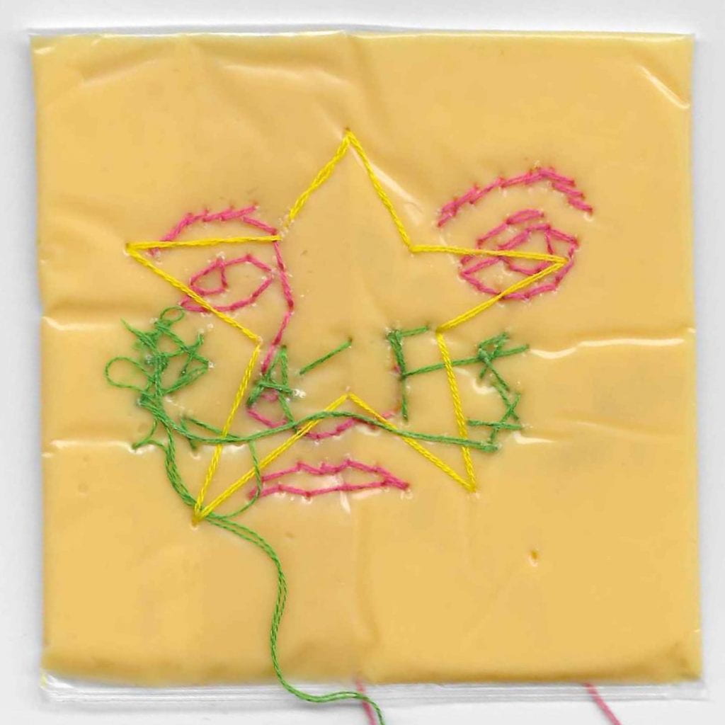 A slice of American cheese with sewed thread forming a face
