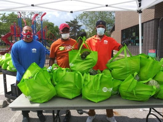 Three volunteers hold green bags full of produce to distribute to needy families.
