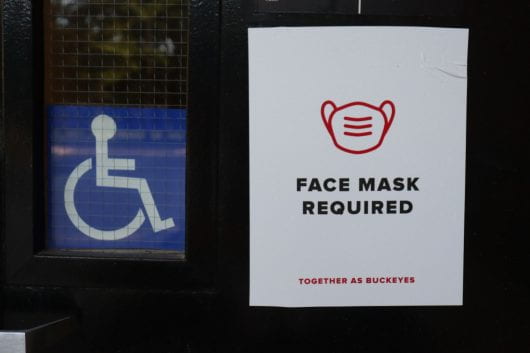 sign on door of building that with image of mask and "face mask required" next to a wheelchair sign