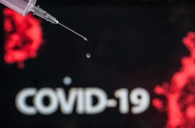 A drip from a syringe in front of a COVID-19 cell