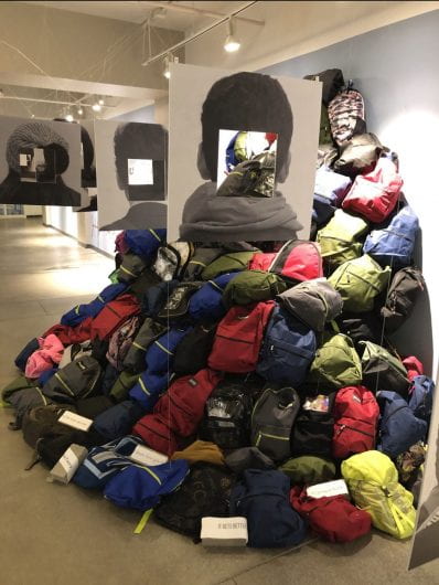 a mound of backpacks stacked on top of eachother against a wall