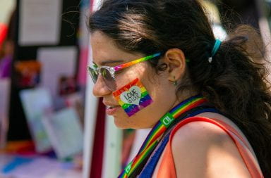 a photograph of a woman at a pride event baring rainbows and a love is love sticker on her face