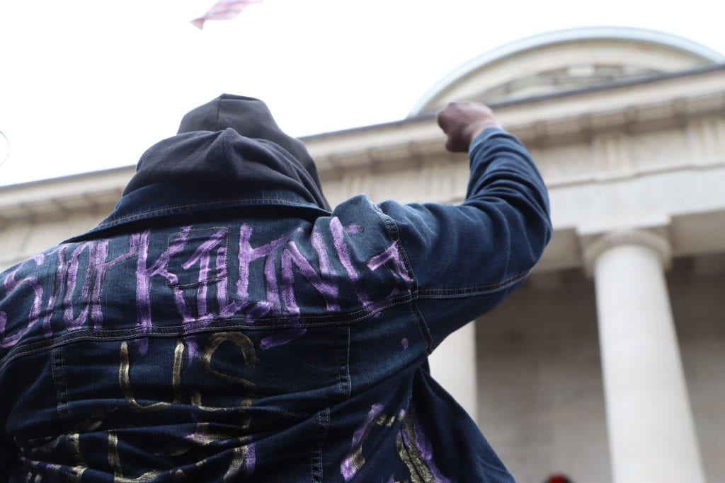 A man wears a jacket that reads "Stop killing us."