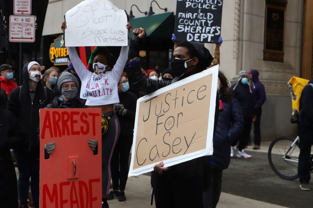 A man holds a sign that says "Justice for Casey." A woman holds one that says "Arrest Meade."