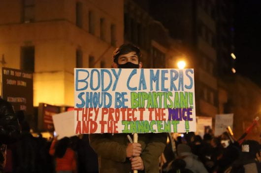a protester holding a sign that reads 'body cameras should be bipartisan. they protect police and the innocent.'