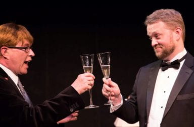 Two men in suits and tuxedo clink champagne flukes with one another to celebrate the awarding of a grant