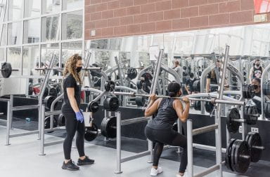 A trainer watches as her client squats the bar