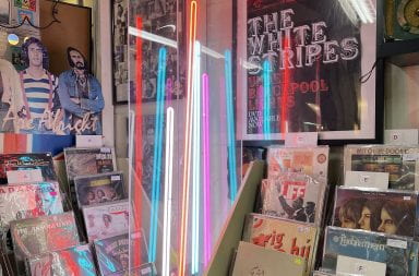 A neon light display sits in a corner between two vinyl record displays