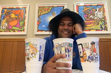 Man poses for a picture with three cups in the foreground