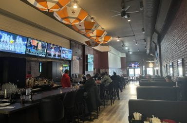 The dining room layout at Downtown Tavern features an open bar and booth and table seating with umbrellas hanging from the ceiling. Credit: Abby Ditmer | Lantern Reporter