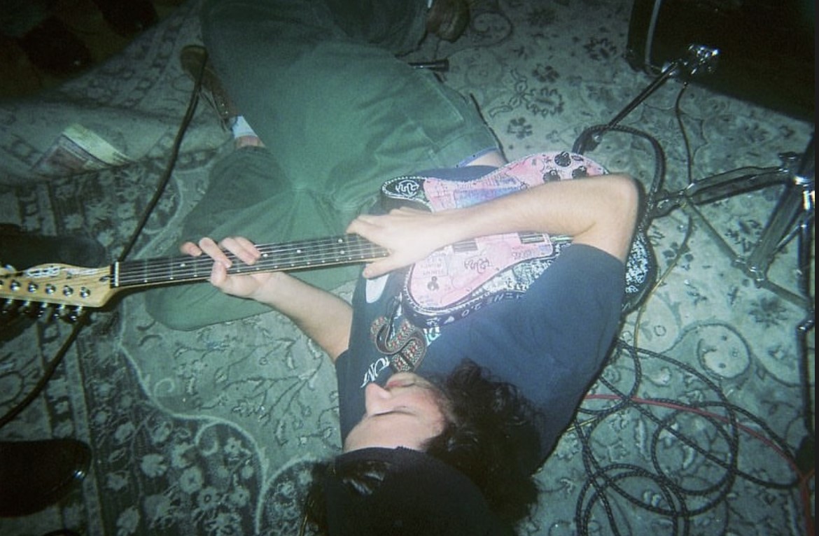 Beck Watson, an Ohio State student and the guitarist of emo band Starling, rolls around on the floor with guitar in hand at Marlboro Manor on Nov. 18, 2023. Credit: Courtesy of Courtney Barger