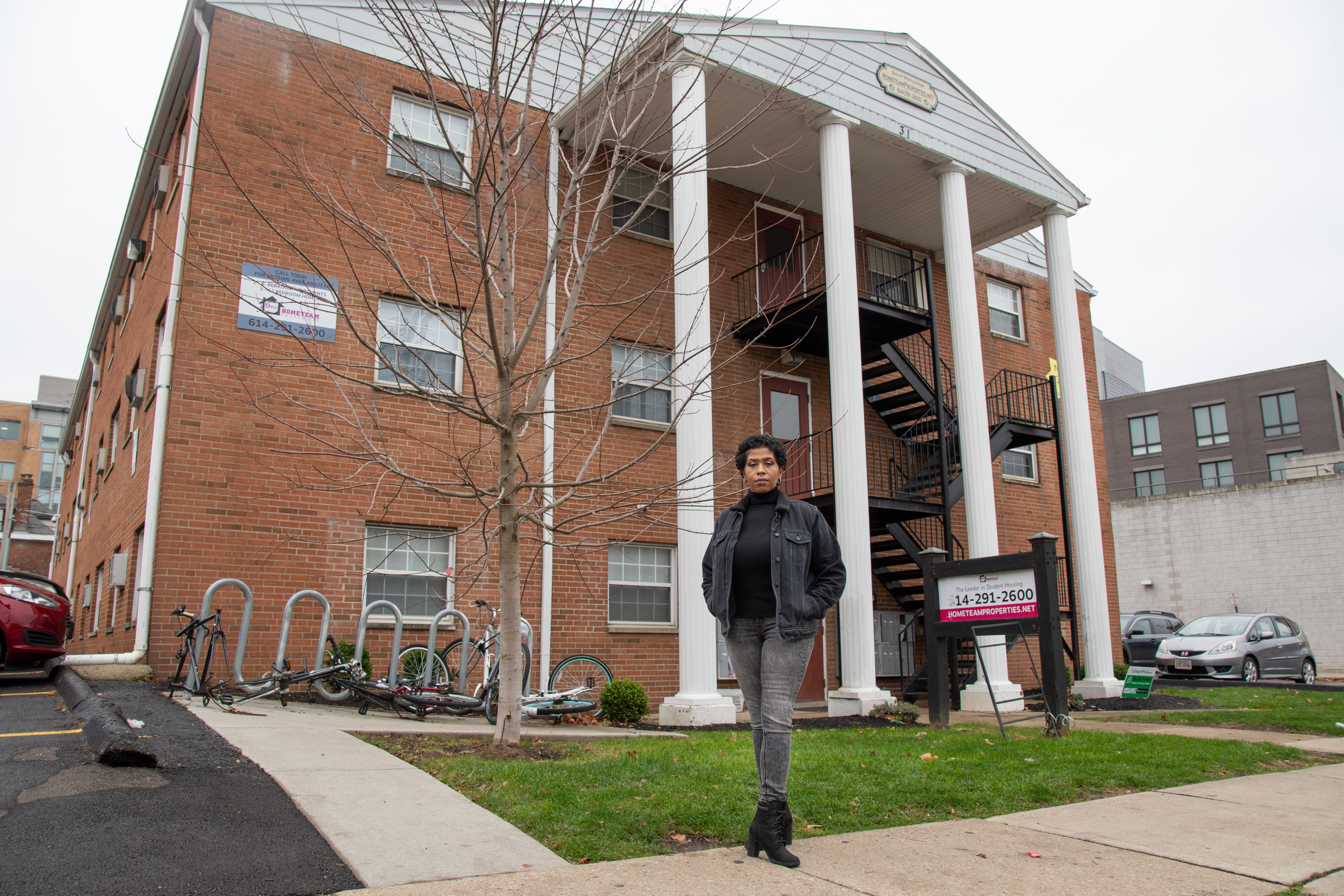 A Black woman stands in front of a brick apartment building