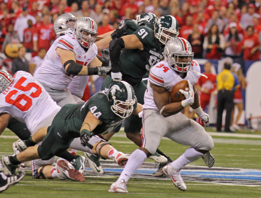 Senior running back Carlos Hyde (34) breaks through the line on a run during the Big Ten Championship Game Dec. 7 in Indianapolis. OSU lost to Michigan State, 34-24. Credit: Shelby Lum / Photo editor