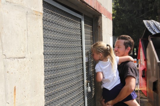 Master's candidate Adrian Waggonner shows his daughter the projection work of fellow artist Lillianna Marie on Aug. 26, 2014. Her work, entitled "Refrain," is observable only through a peephole on a shed outside Ramseyer Hall. Credit: Daniel Bendtsen / Asst. arts editor