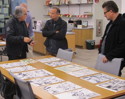 Patrons of Cartoon Crossroads gather around a table with artists' work laid out on it during the show in 2015. Credit: Courtesy of Cartoon Crossroads Columbus